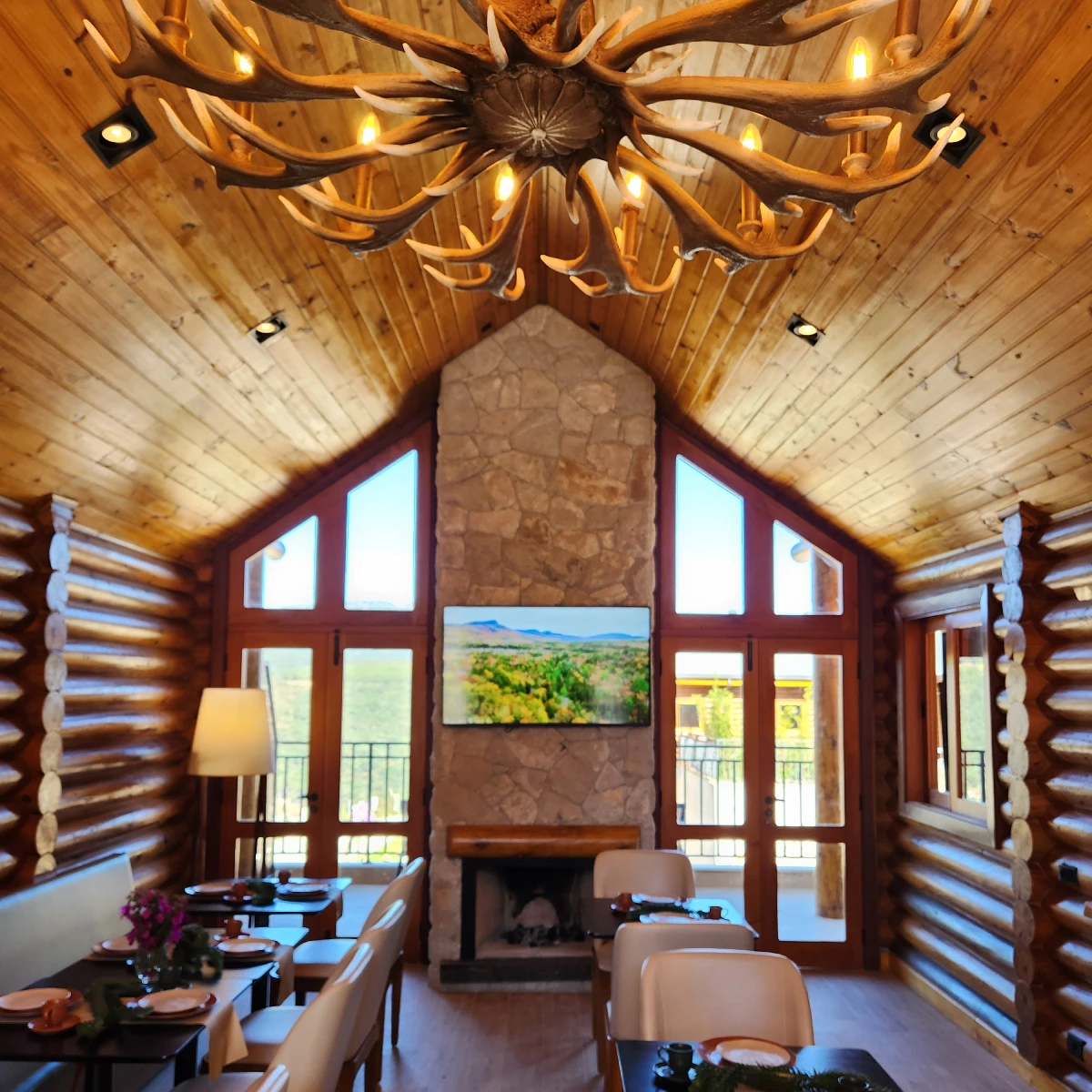 Sala de estar da Pousada Maple com pé-direito alto em madeira, lareira e janelas voltadas para o vale